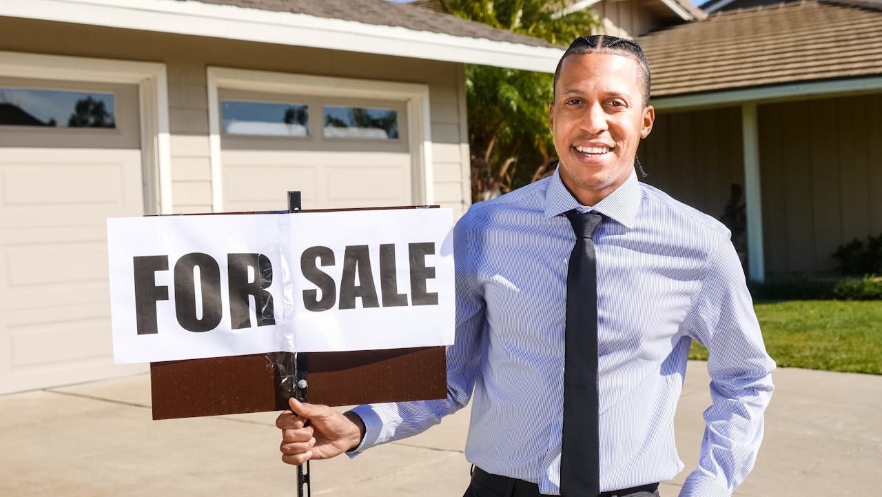 services-02 Smiling real estate agent with a for sale sign in front of a house.