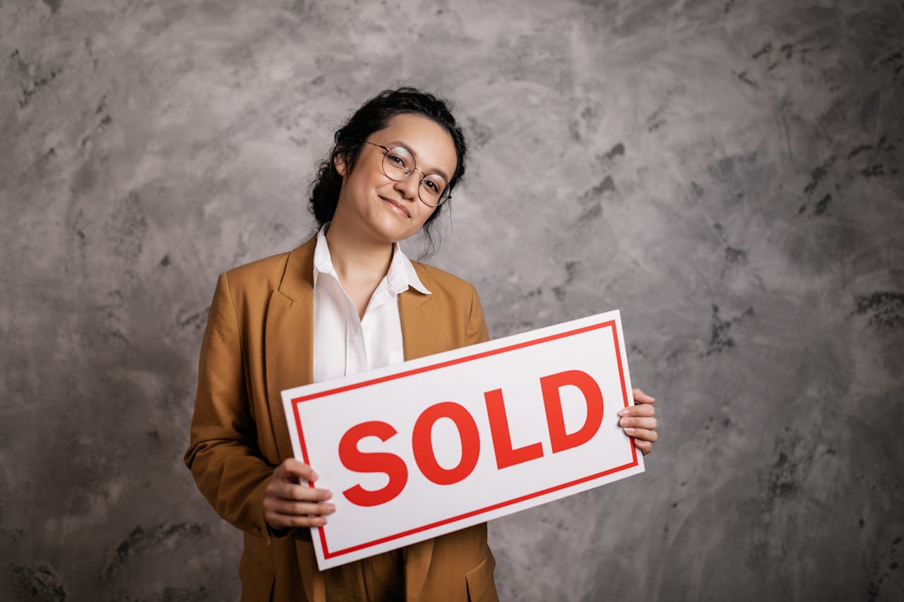 services-02 Confident real estate agent holding a 'Sold' sign indoors, symbolizing successful property sale.