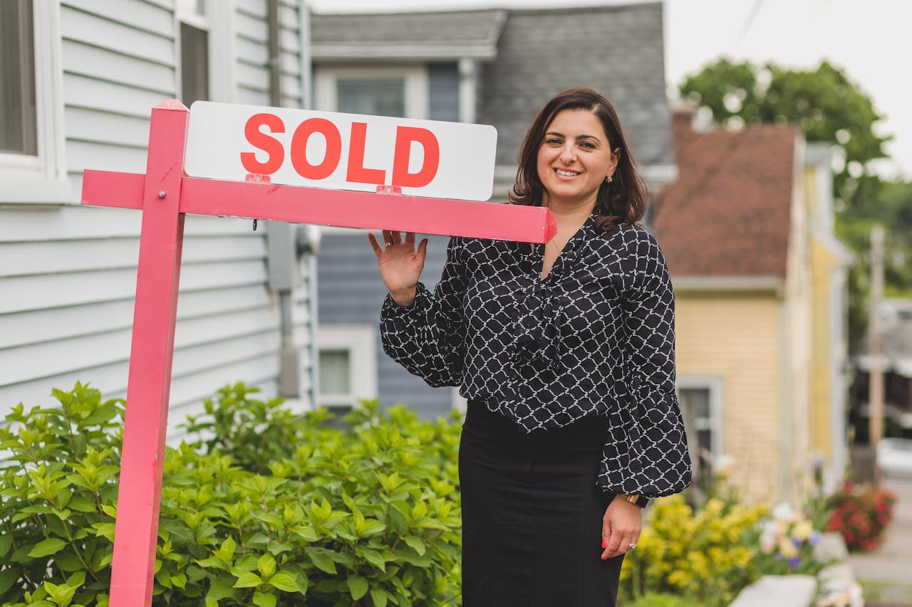 our-experience Smiling real estate agent standing outdoors with a sold sign, symbolizing success and achievement in property sales.